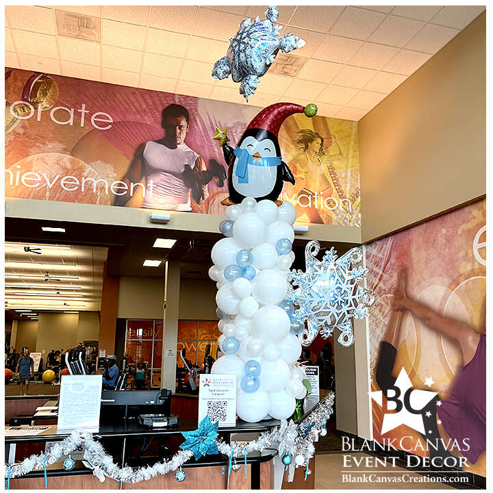 Organic style winter balloon column with white, silver and light blue balloons with a penguin on top with floating snowflake balloon